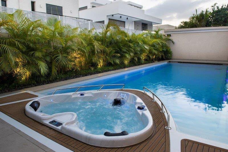 Heart shaped 2-person hot tub on wooden deck beside pool, surrounded by tropical palms - Passion Spas Signature Collection Hot Tubs