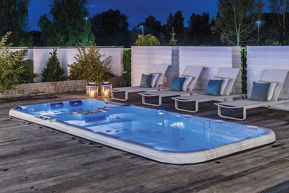 Illuminated Dynamic swim spa on wooden deck with loungers at dusk, featuring blue LED lighting - Passion Spas Sport Collection