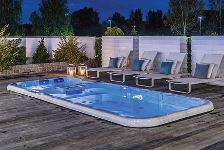 Illuminated Dynamic swim spa on wooden deck with loungers at dusk, featuring blue LED lighting - Passion Spas Sport Collection